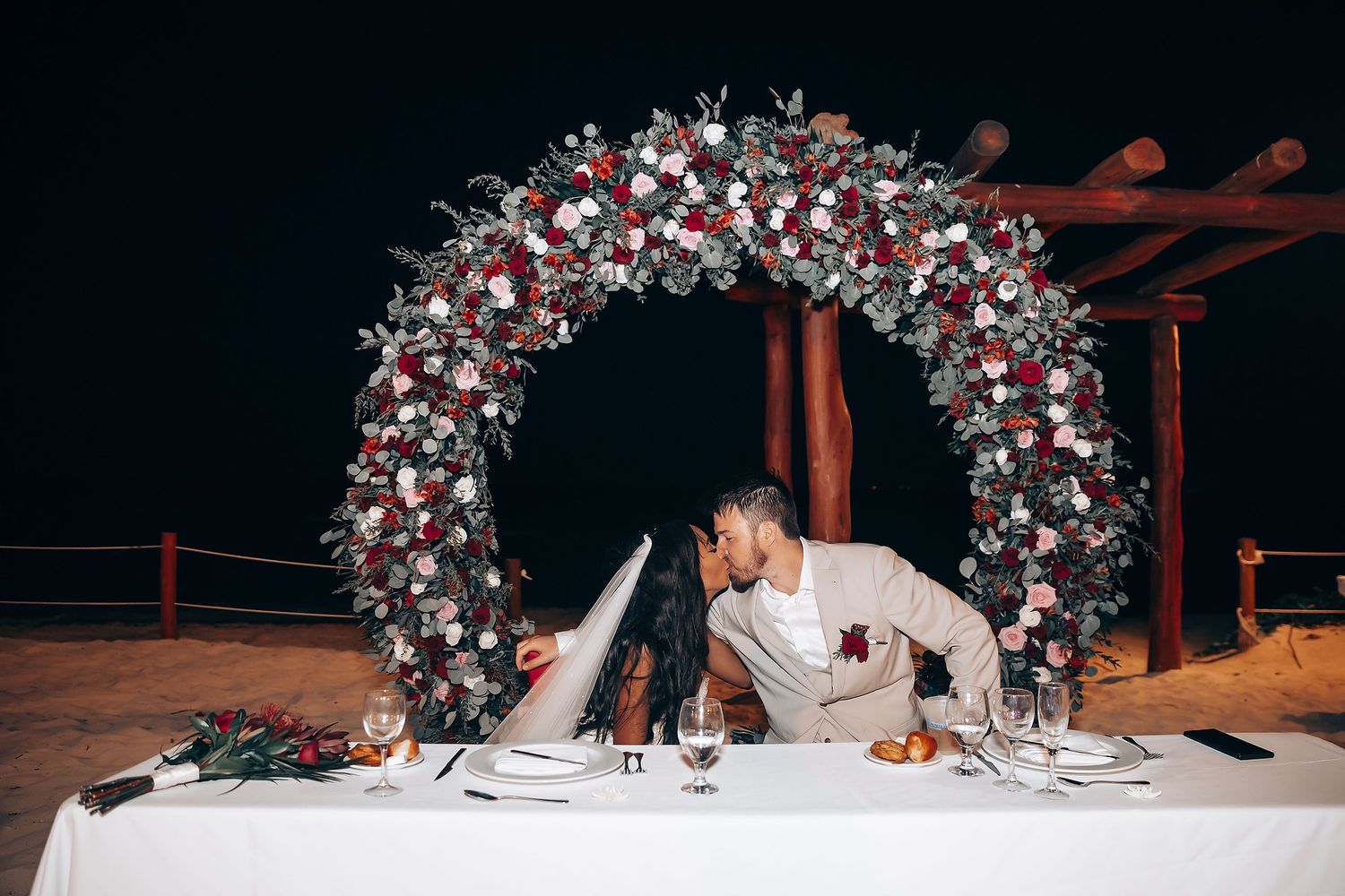 Wedding reception table decorated with elegant floral arch and romantic lighting.