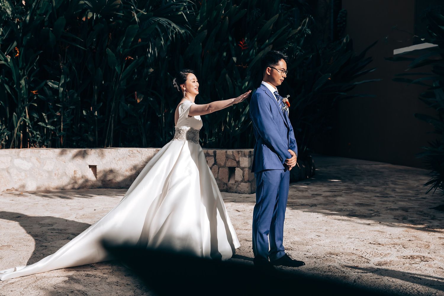 Wedding couple poses against rustic stone walls in a garden setting.