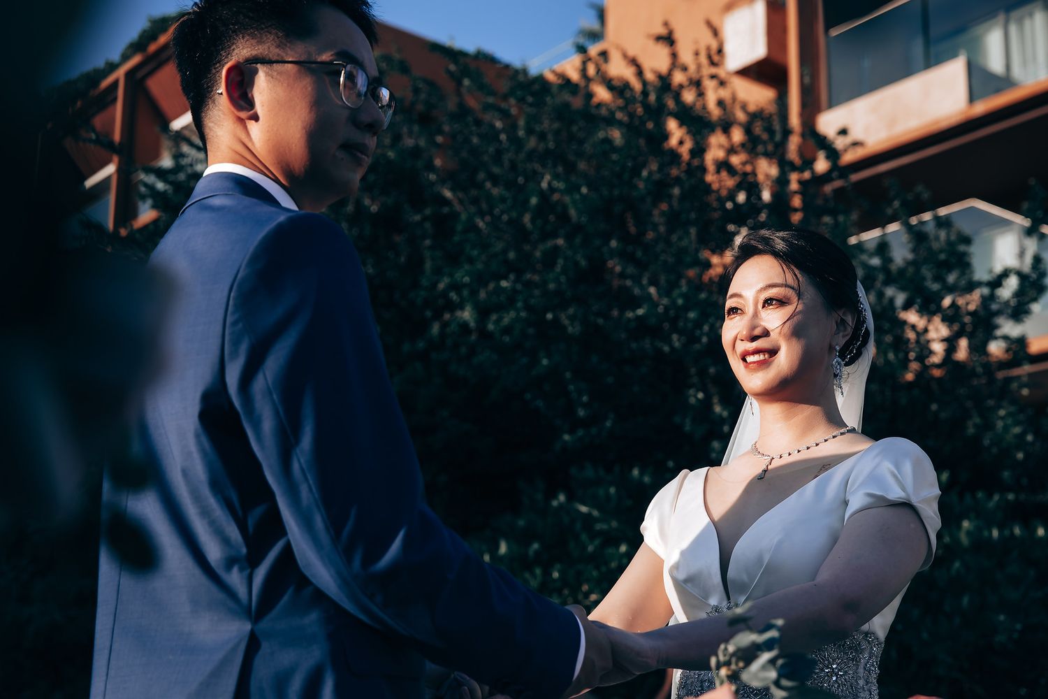 Couple shares romantic moments in a garden setting with blooming coral roses and lush greenery.