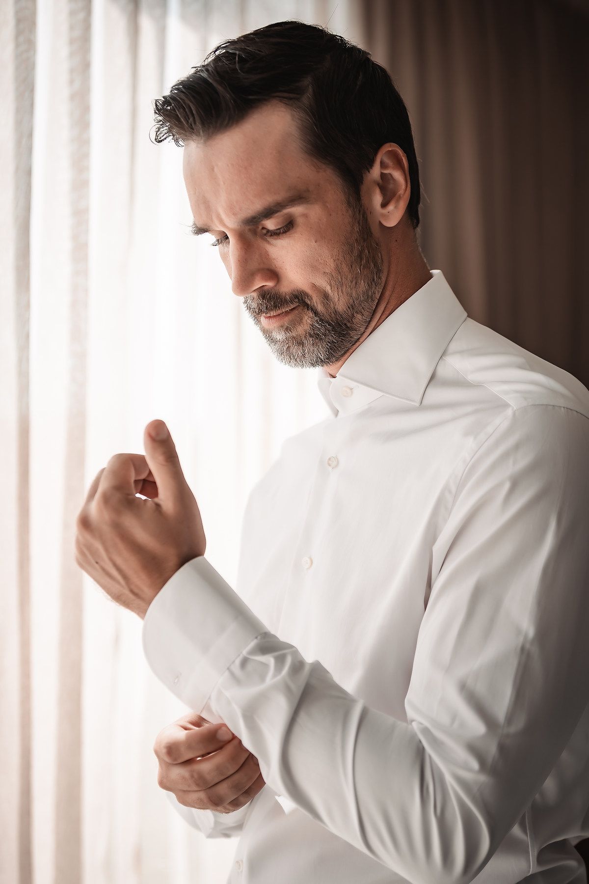 Sequence of groom getting ready shots showing final touches on white dress shirt.
