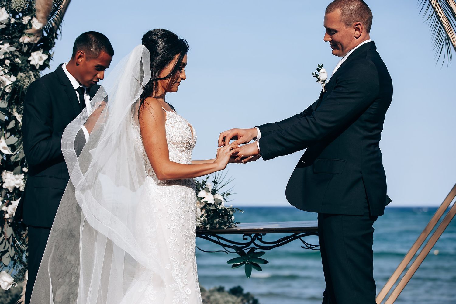 An intimate beachfront wedding ceremony with palm trees and ocean waves in the background.