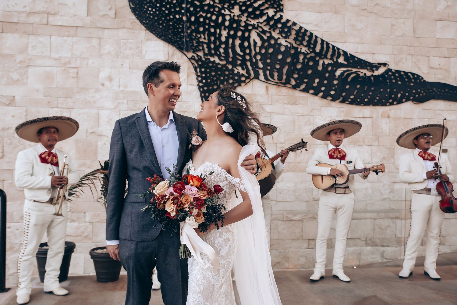 Wedding celebration with mariachi band performing against stone wall backdrop.