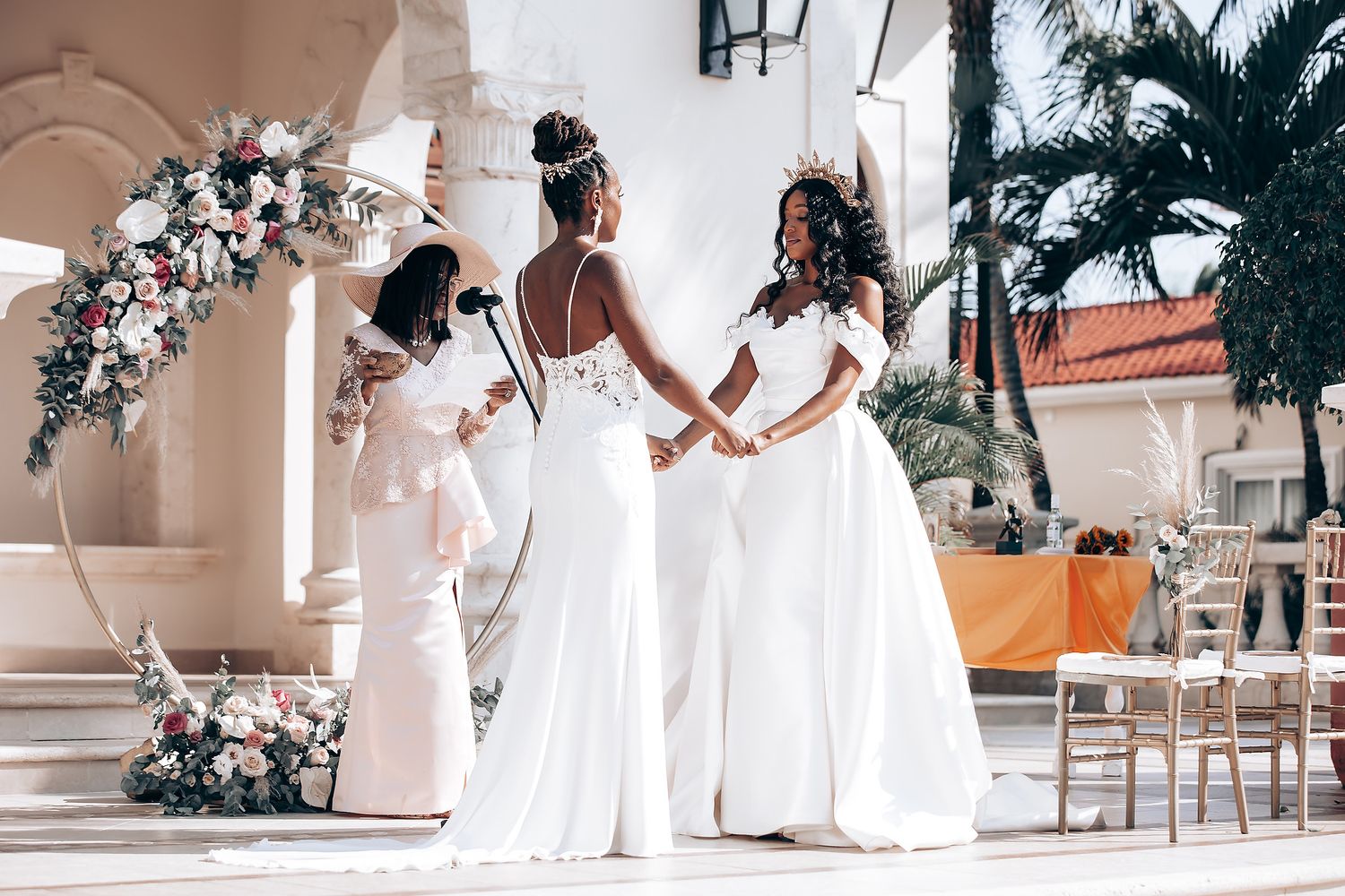 Wedding party in white dresses posing along an elegant colonnade with palm trees.