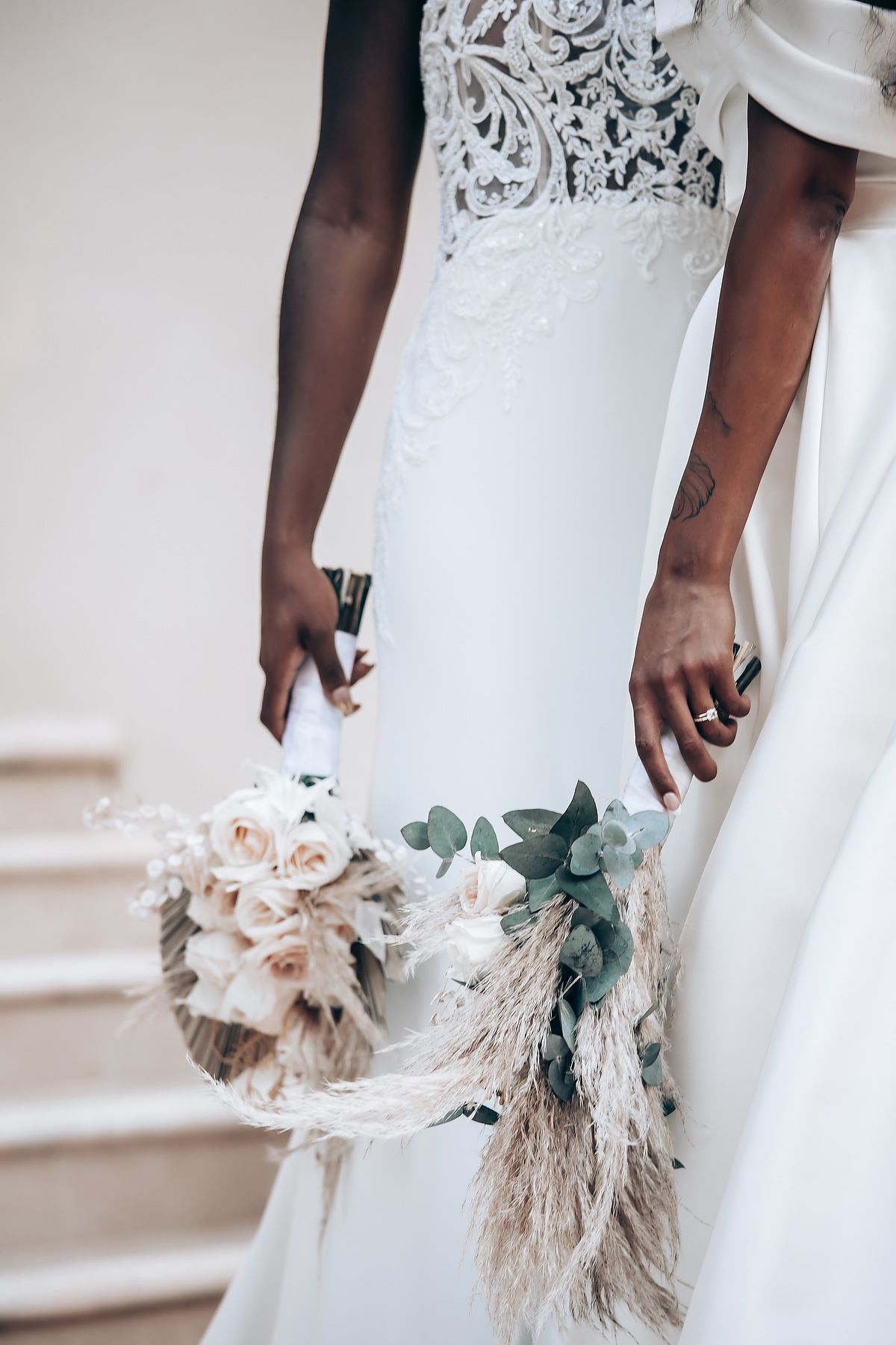 Detail of white lace wedding dress with romantic bouquet of roses and pampas grass.