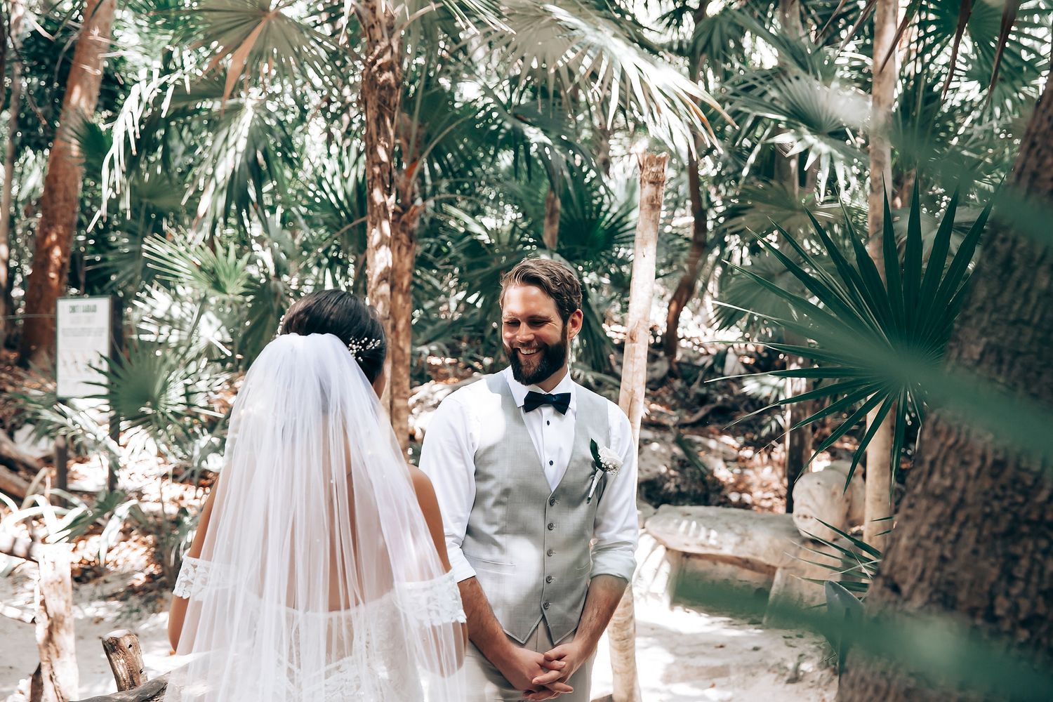 Guests gather under palm trees for a tropical beach wedding ceremony.