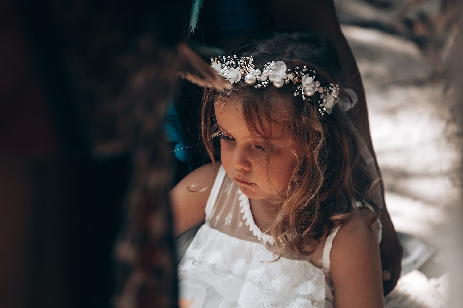 A bride wearing a delicate floral crown and white lace dress gazes downward in soft, ethereal lighting.