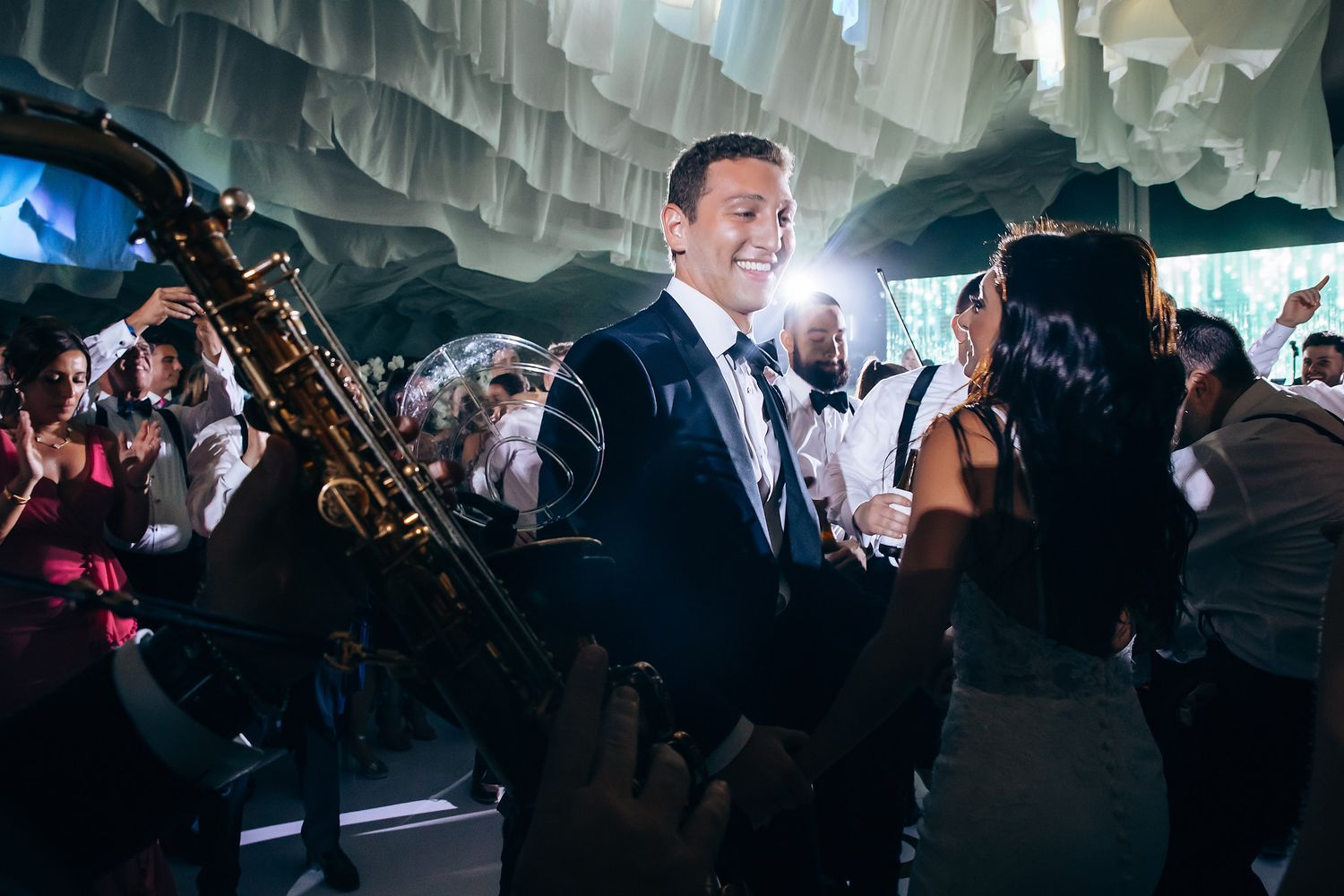 A lively wedding reception under draped fabric with a saxophone player.
