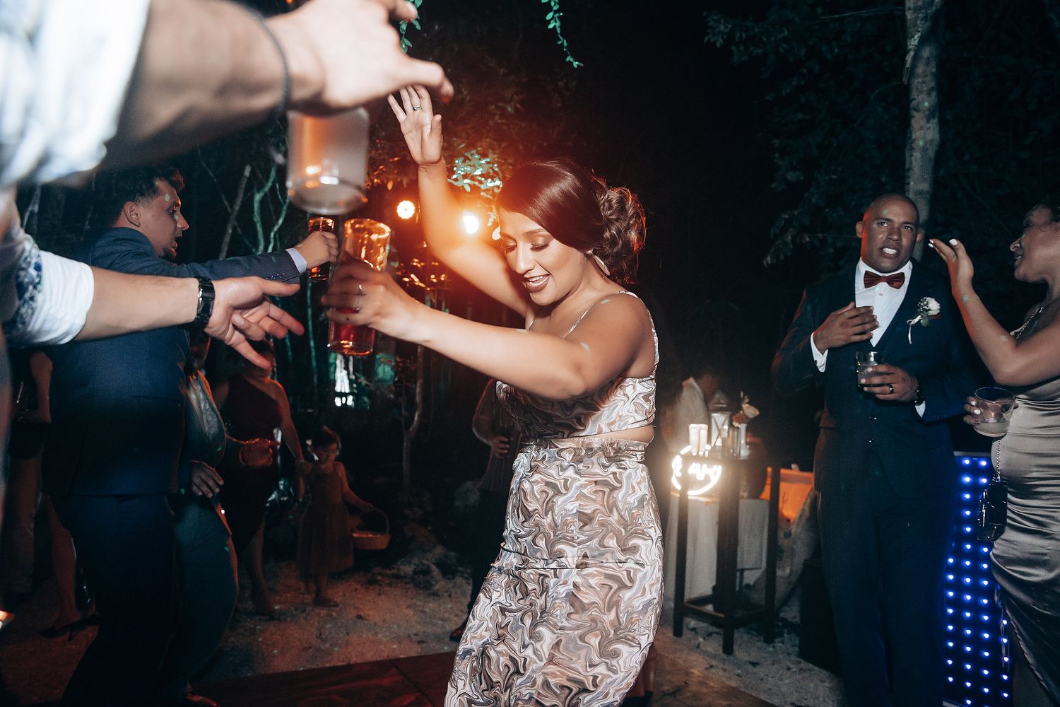 A couple dancing at a nighttime wedding celebration with sparklers and guests surrounding them.