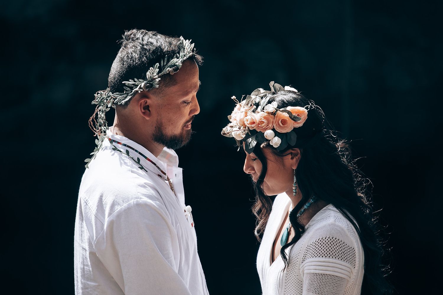 Couple in white attire sharing an intimate moment in a forest setting.