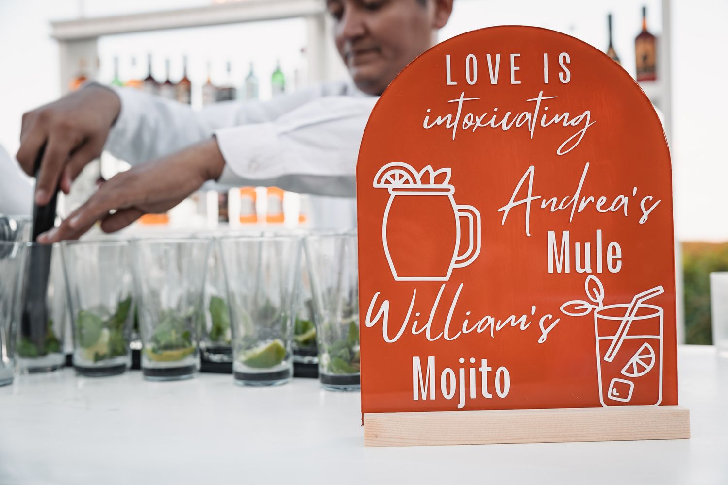 Custom wedding bar sign reading Love Is Intoxicating with personalized cocktail names for couple.