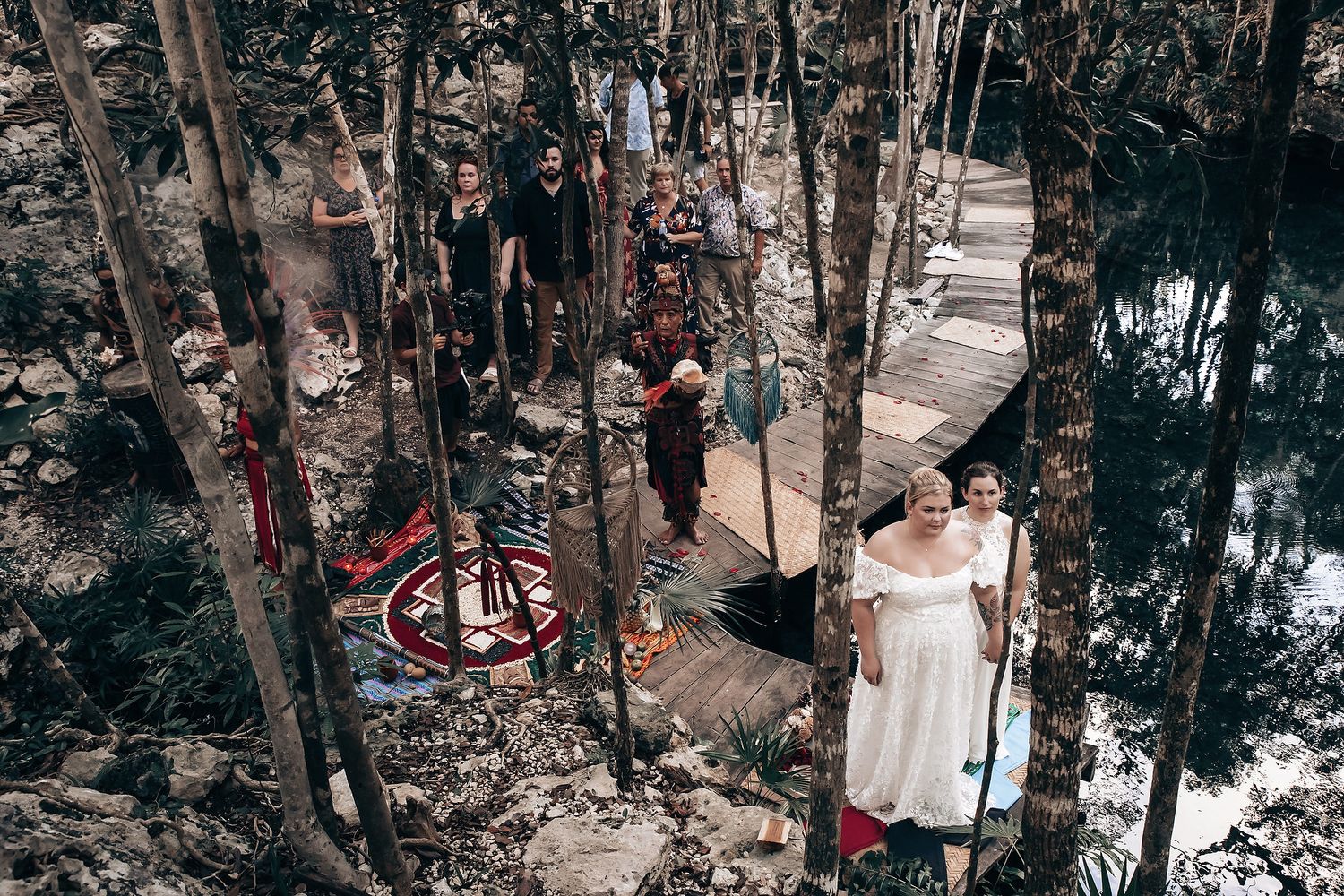 The image shows a group of people, including a bride and groom, walking on a path in a forested area.