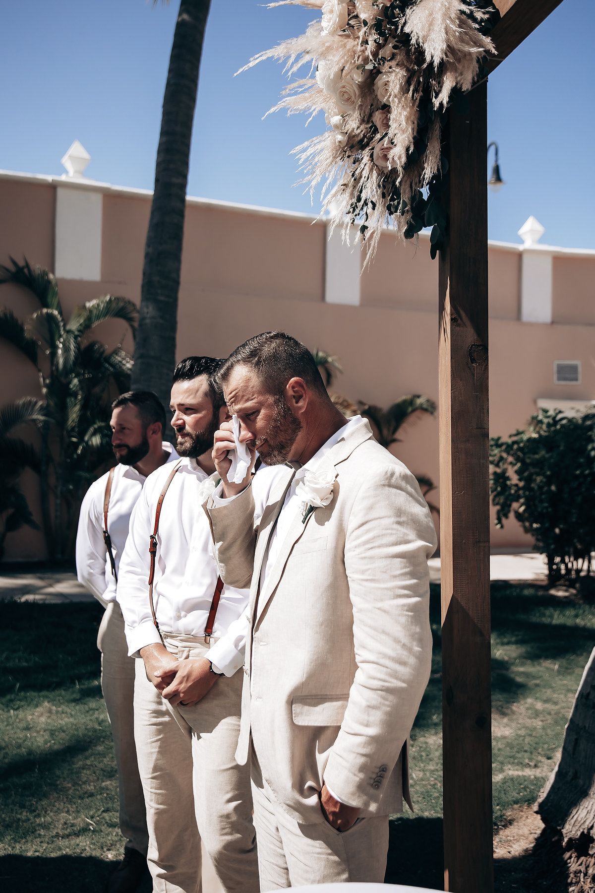 A group of men in white suits standing together in an outdoor setting with palm trees.