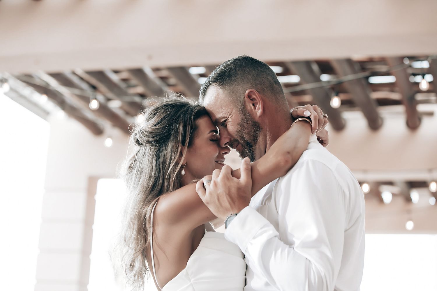 A couple embracing and kissing in an outdoor setting with a thatched roof structure.