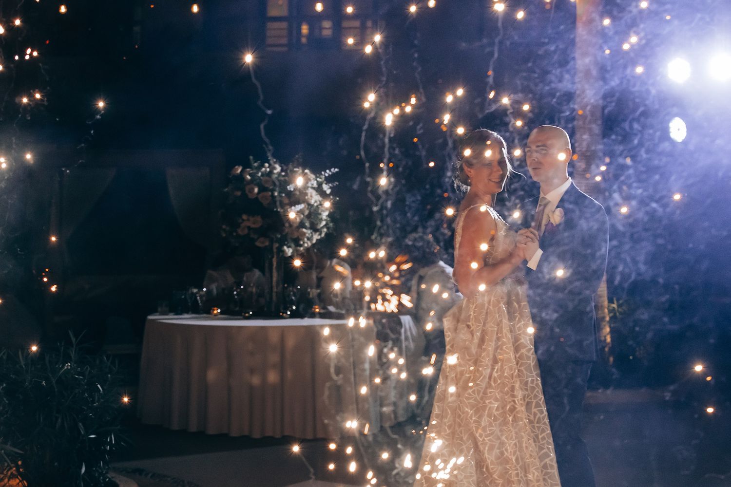 A bride and groom stand together amidst a display of twinkling lights.