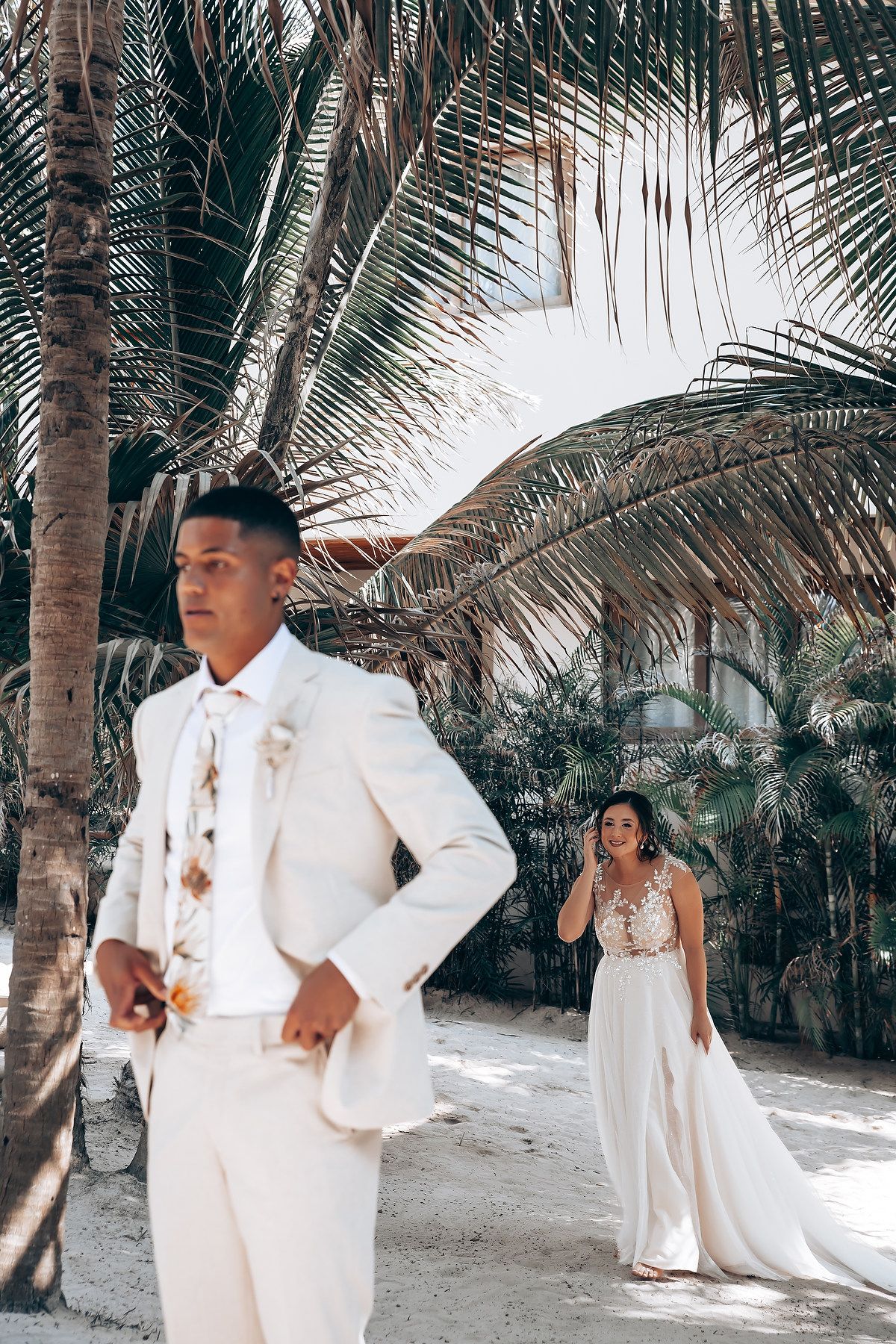 Beach wedding scene with palm trees and guests in white formal attire.