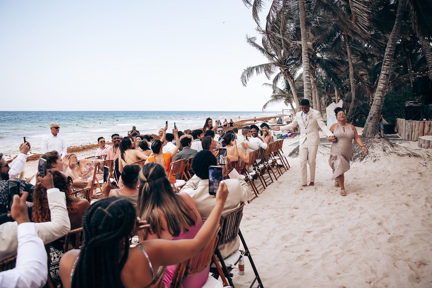Beach wedding ceremony setup with guests seated in white chairs facing the ocean.