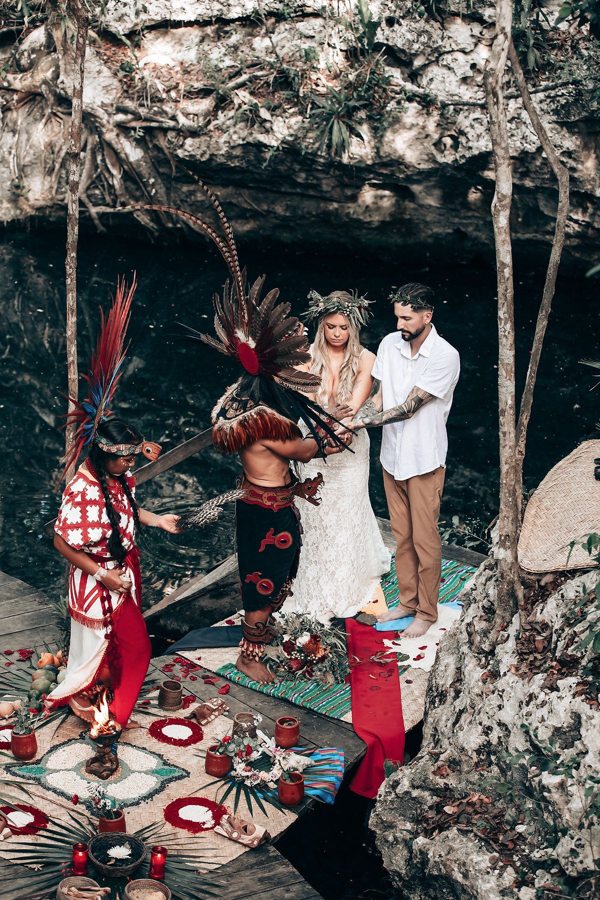 Traditional ceremony performers in red and white attire conduct rituals in a natural cave setting.