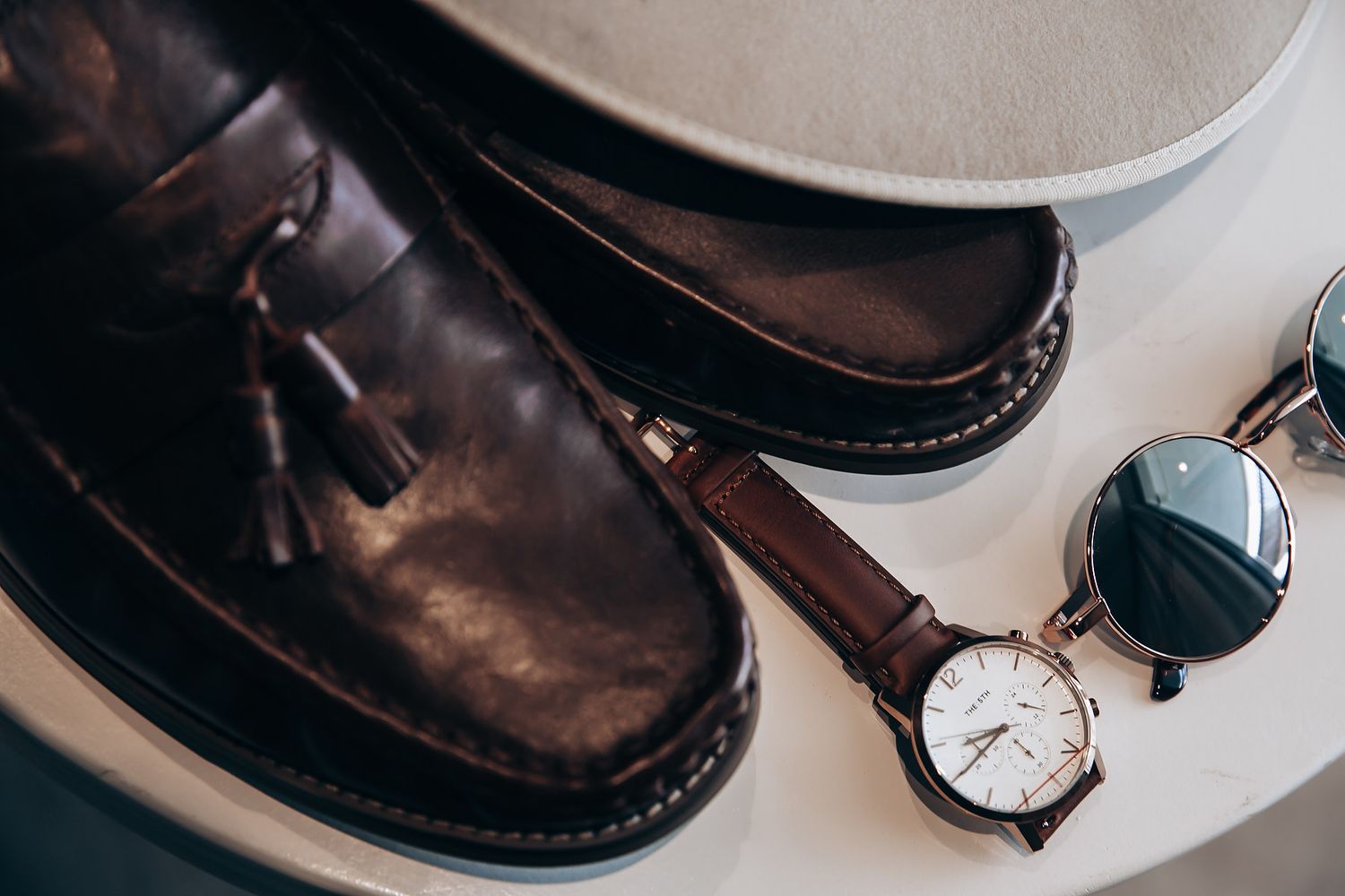 Classic leather dress shoes and wristwatch arranged on beige surface.