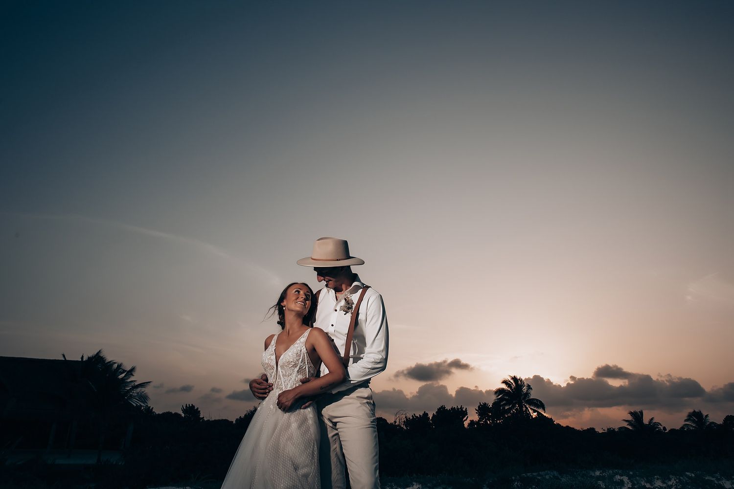Silhouetted wedding couple against a dusky tropical beach backdrop.