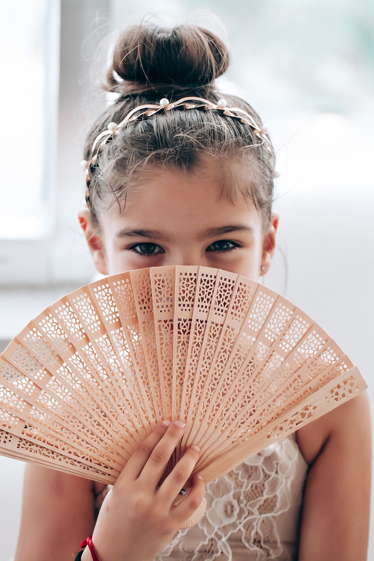 Delicate lace fan held playfully in front of a white lace dress.