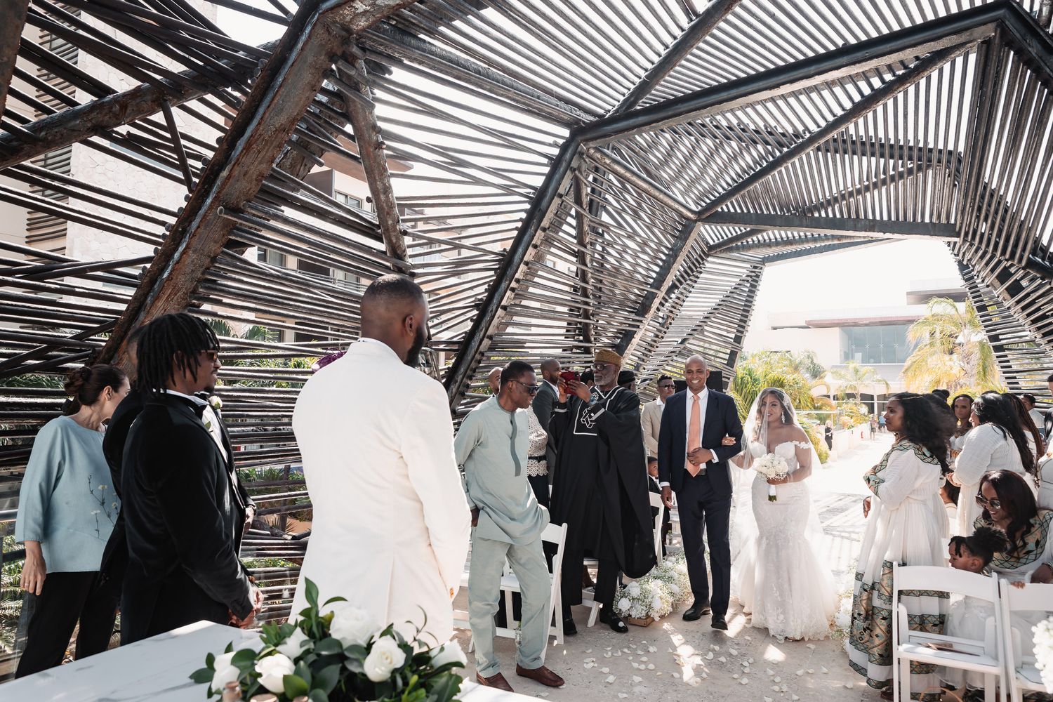 Wedding ceremony under rustic wooden pergola with guests watching bride walk down aisle.