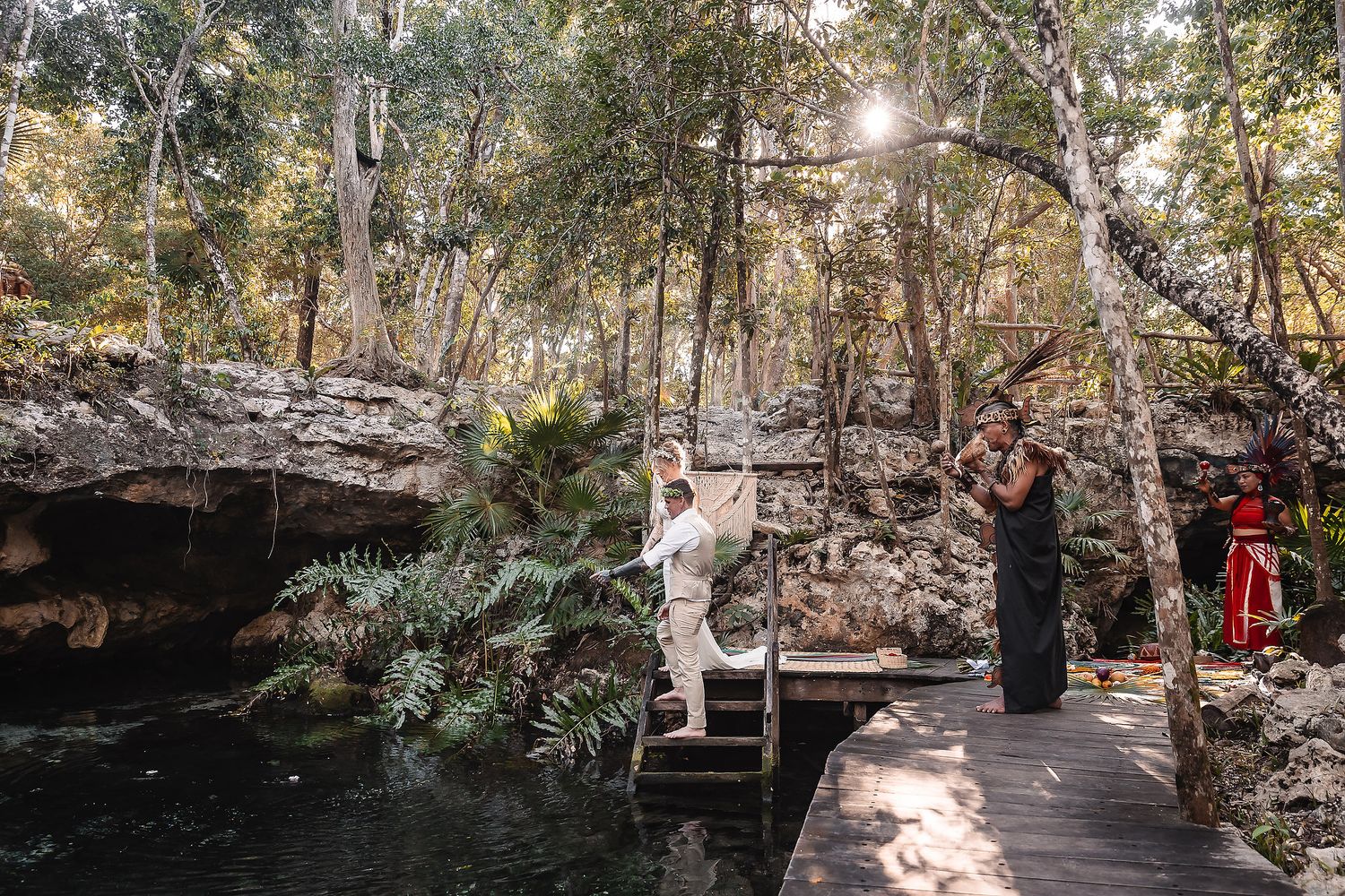 Bride and groom celebrate at a scenic cenote wedding in a sunlit jungle forest with wooden walkway and lush greenery.