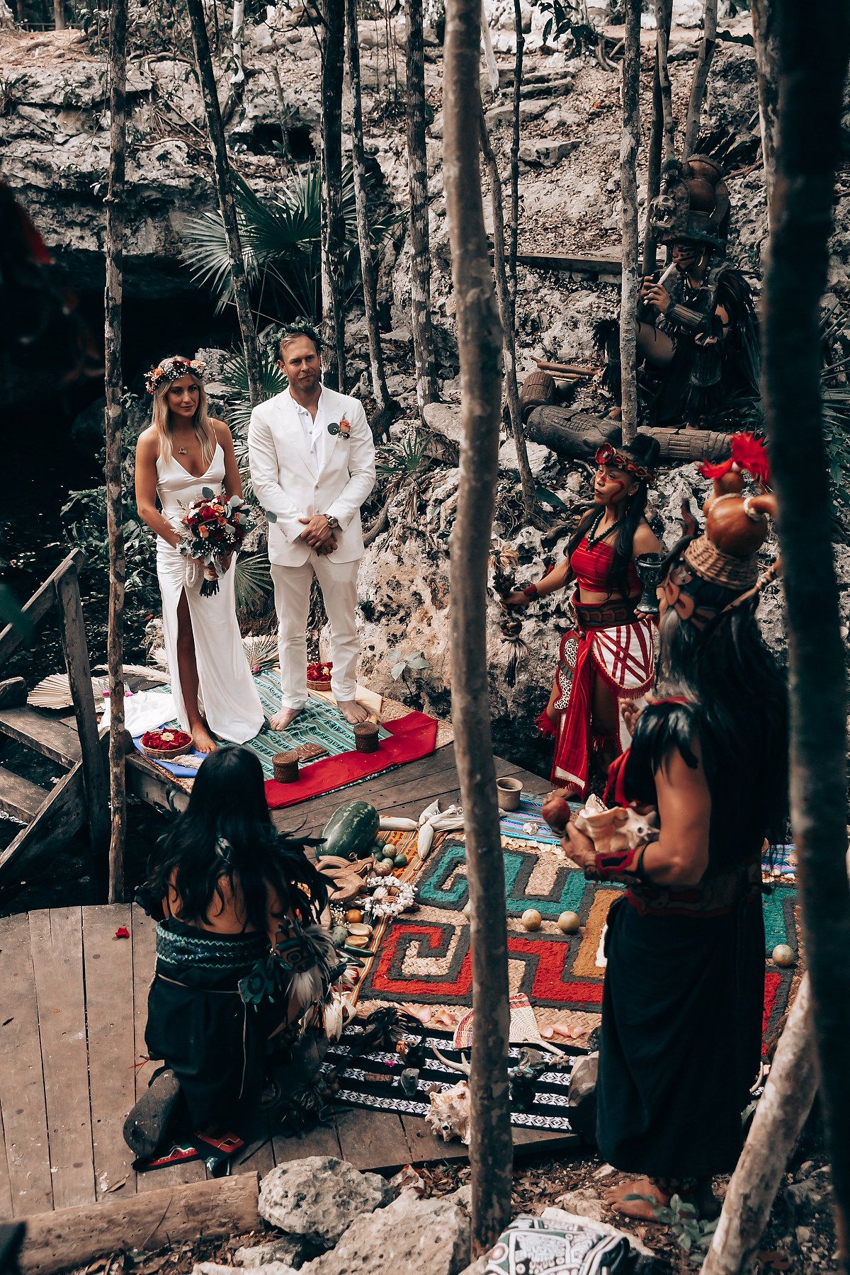 Wedding guests gather in a forest setting with blankets and cushions for an intimate outdoor ceremony.