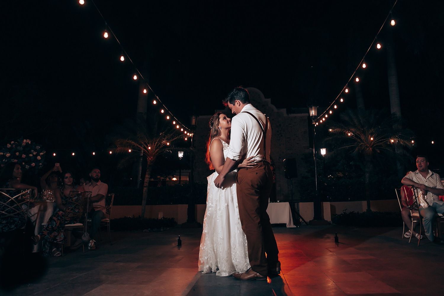 Wedding reception dance floor illuminated by romantic string lights at night.