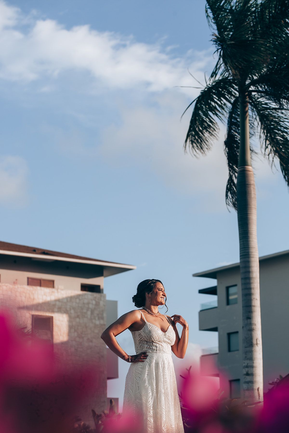 A white wedding dress silhouetted against a tropical sky with palm trees and buildings.