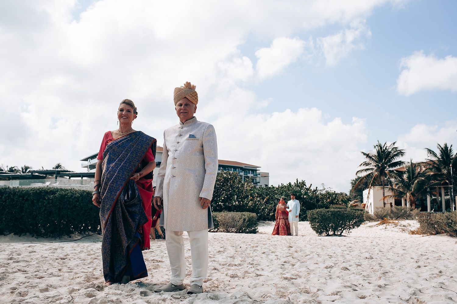Wedding party members walk along a pristine white sand beach with palm trees in the background.