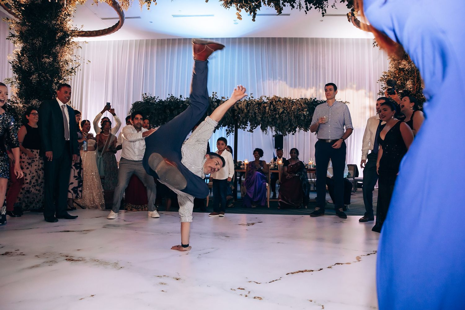 Wedding guest performs energetic dance move during reception celebration.
