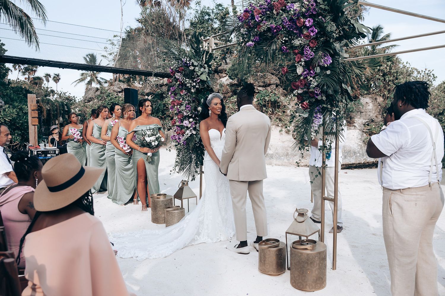 Wedding ceremony setup with white chairs and floral arrangements under palm trees.
