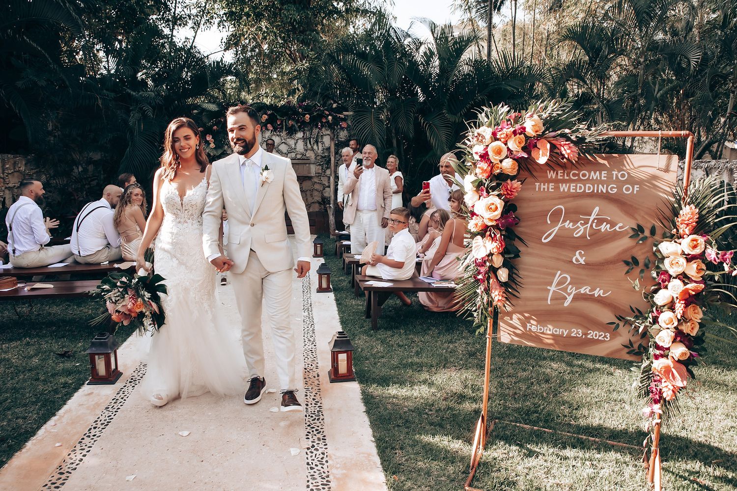 Outdoor wedding ceremony setup with wooden signs and pink floral arch decorations in a garden setting.