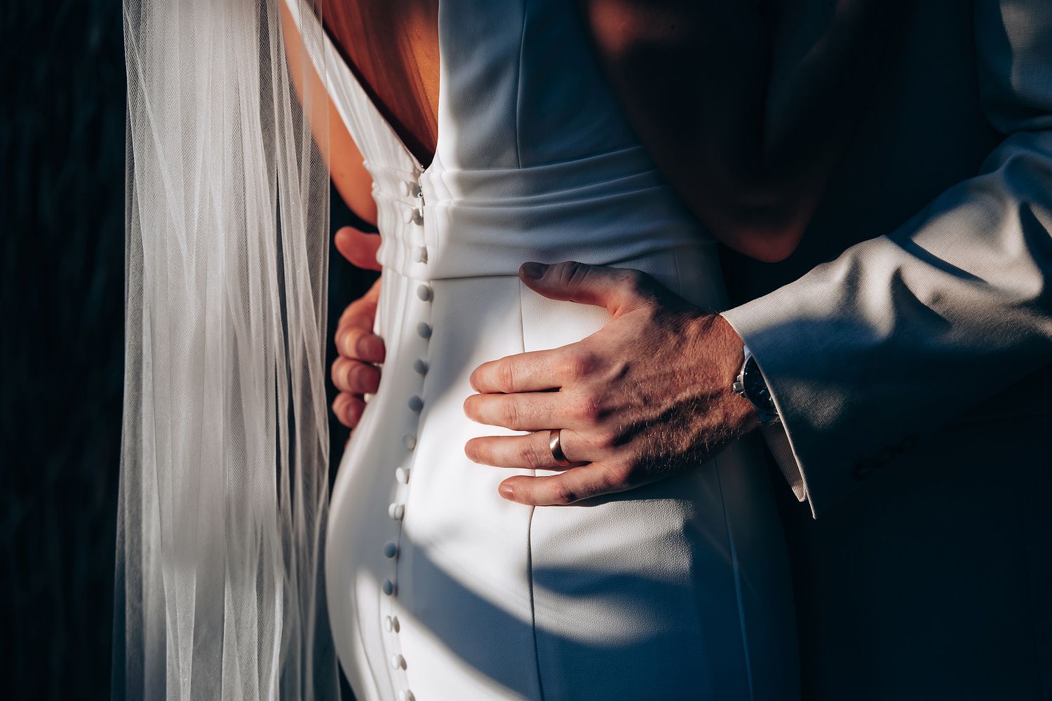 Close-up detail shot of a sleek white wedding dress in dramatic lighting.
