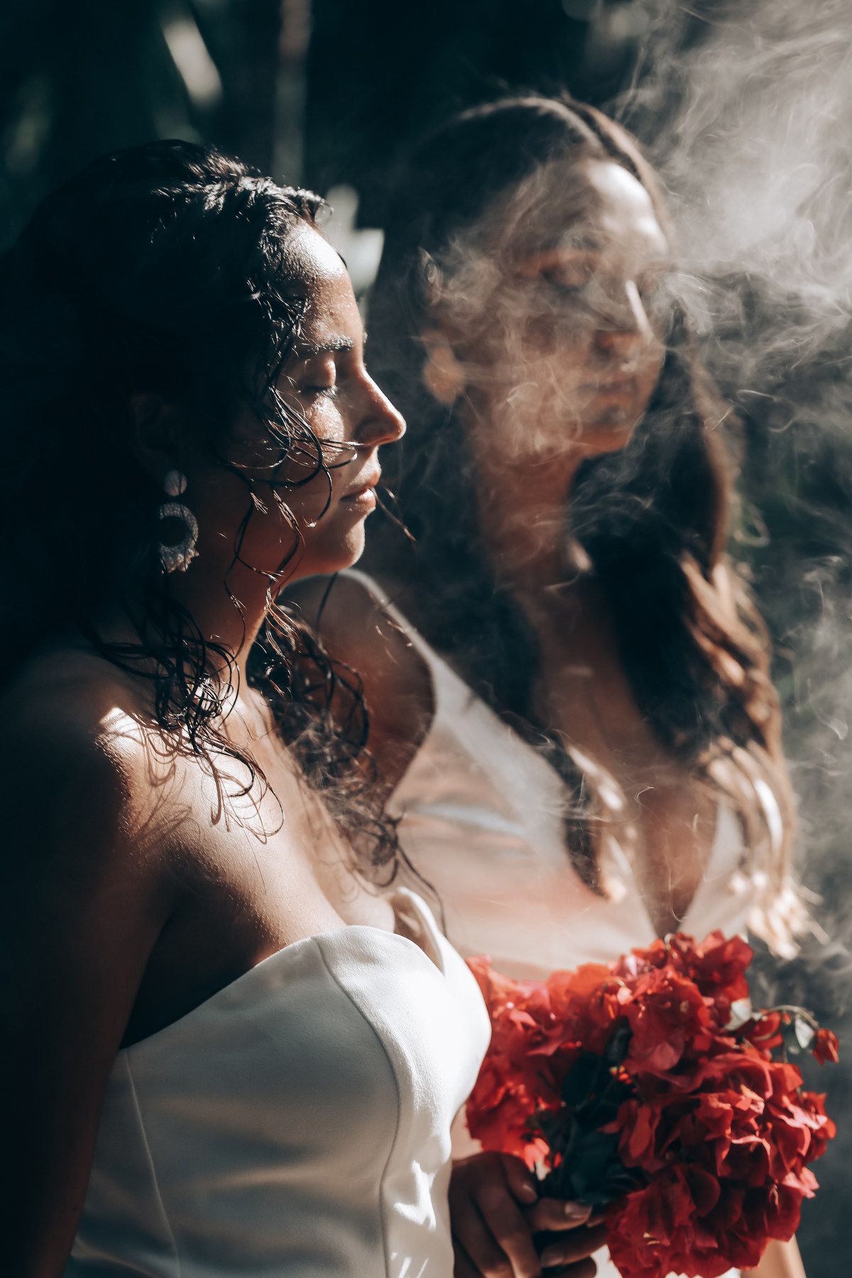 A person in white dress holds vibrant red flowers while smoke or mist creates a dreamy atmospheric effect.