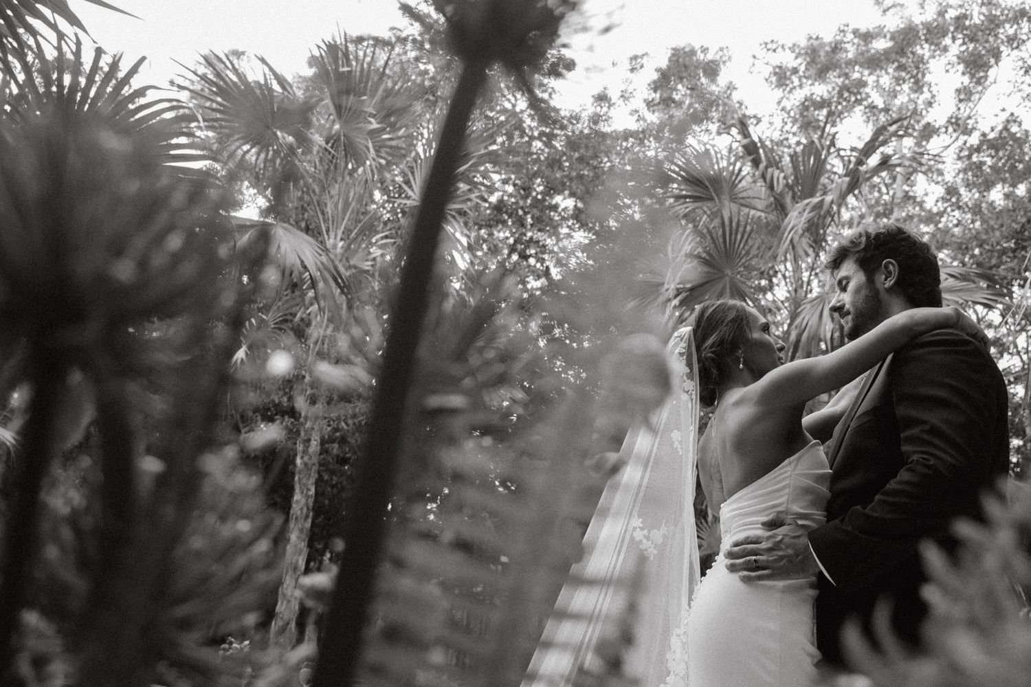 Black and white photo of a couple embracing in a lush tropical garden on their wedding day.