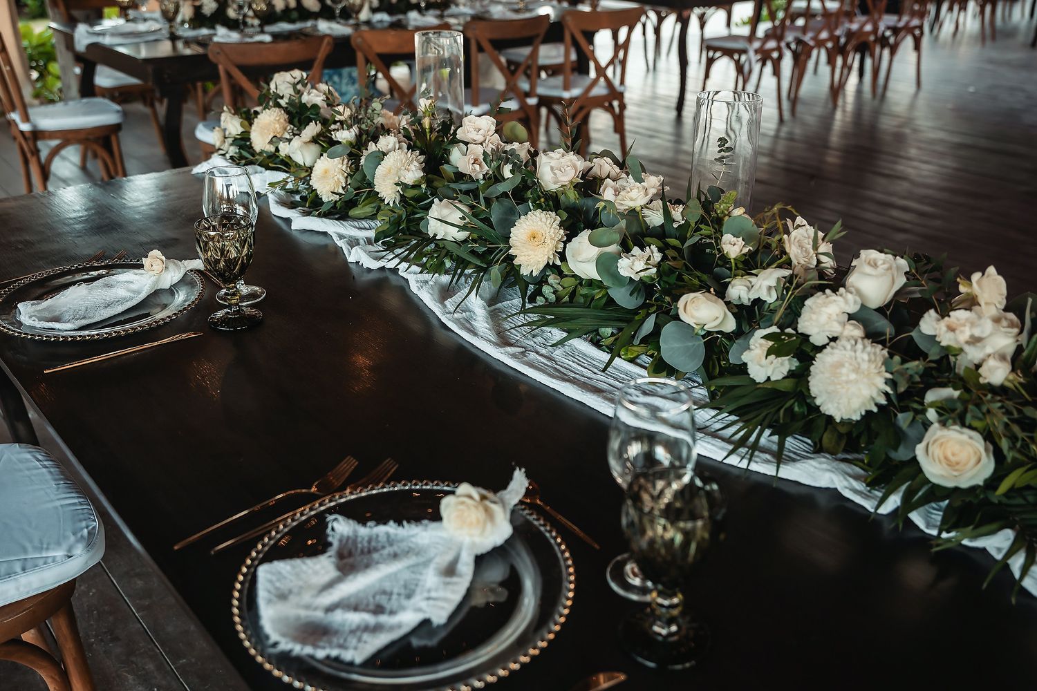 Elegant wedding reception table with white floral centerpiece, gold charger plates, and crystal glassware.