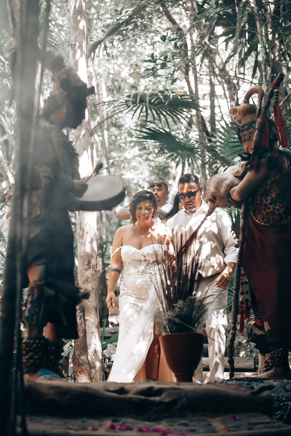 A couple shares a romantic moment in a dreamy forest setting with sunlight filtering through the trees.
