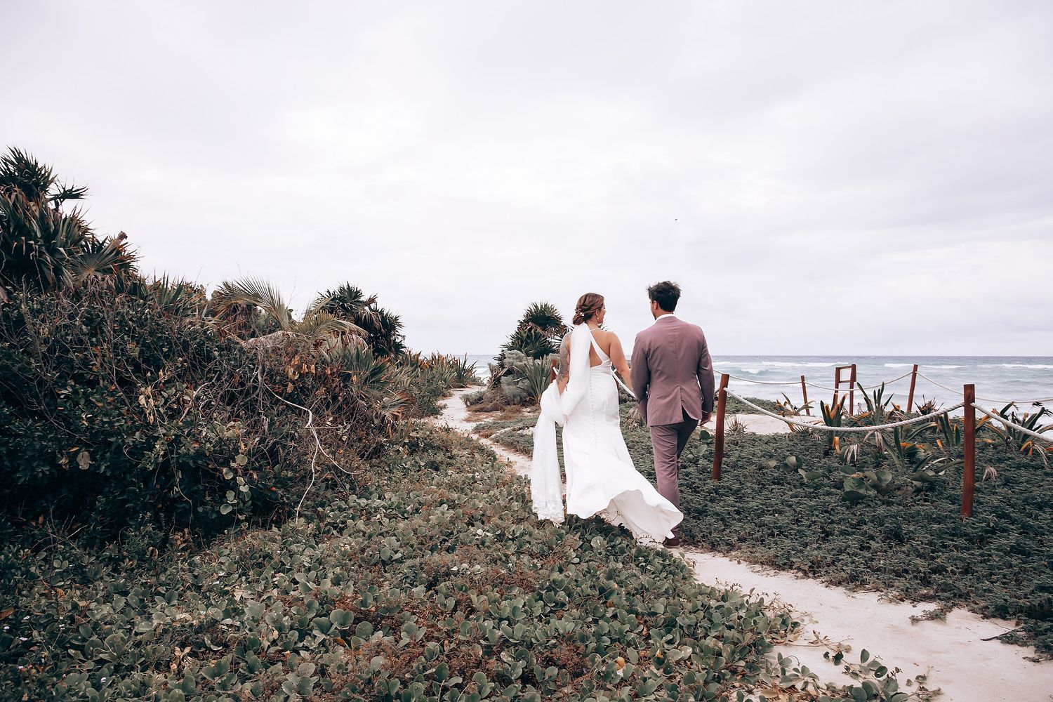 Newlyweds walk hand in hand along a scenic coastal pathway.