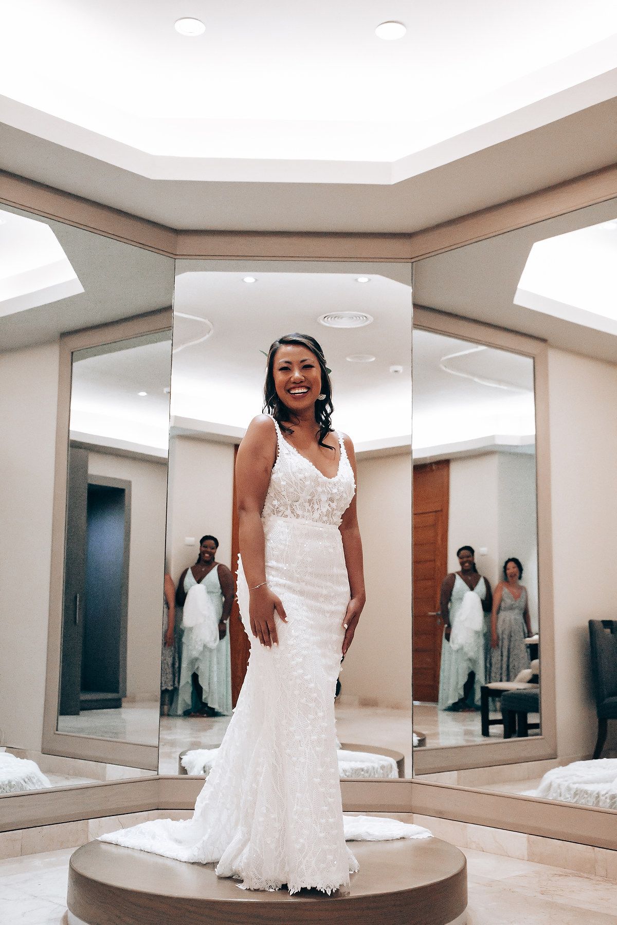 Beautiful white lace wedding dress shown in a bridal fitting room with mirrored walls and elegant lighting.
