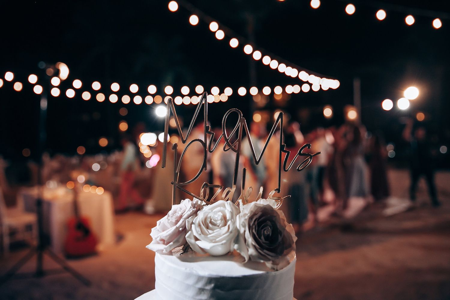 String lights create a magical bokeh effect over an outdoor nighttime wedding celebration.