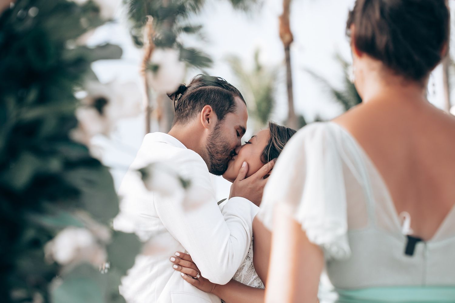 Intimate beach wedding ceremony with white floral arrangements and guests seated.