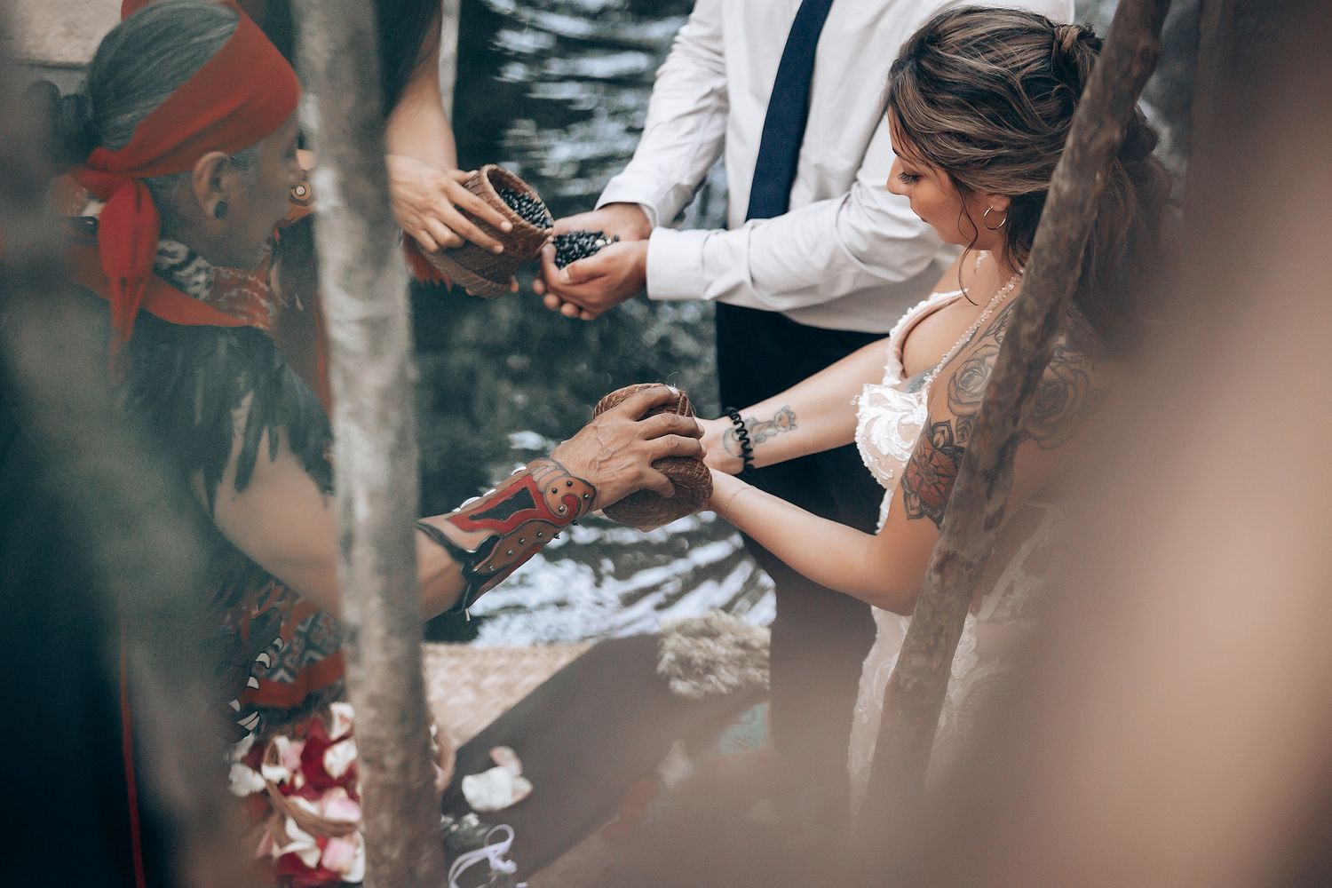Intimate outdoor wedding ceremony with guests gathered around colorful blankets and decorations in a natural setting.