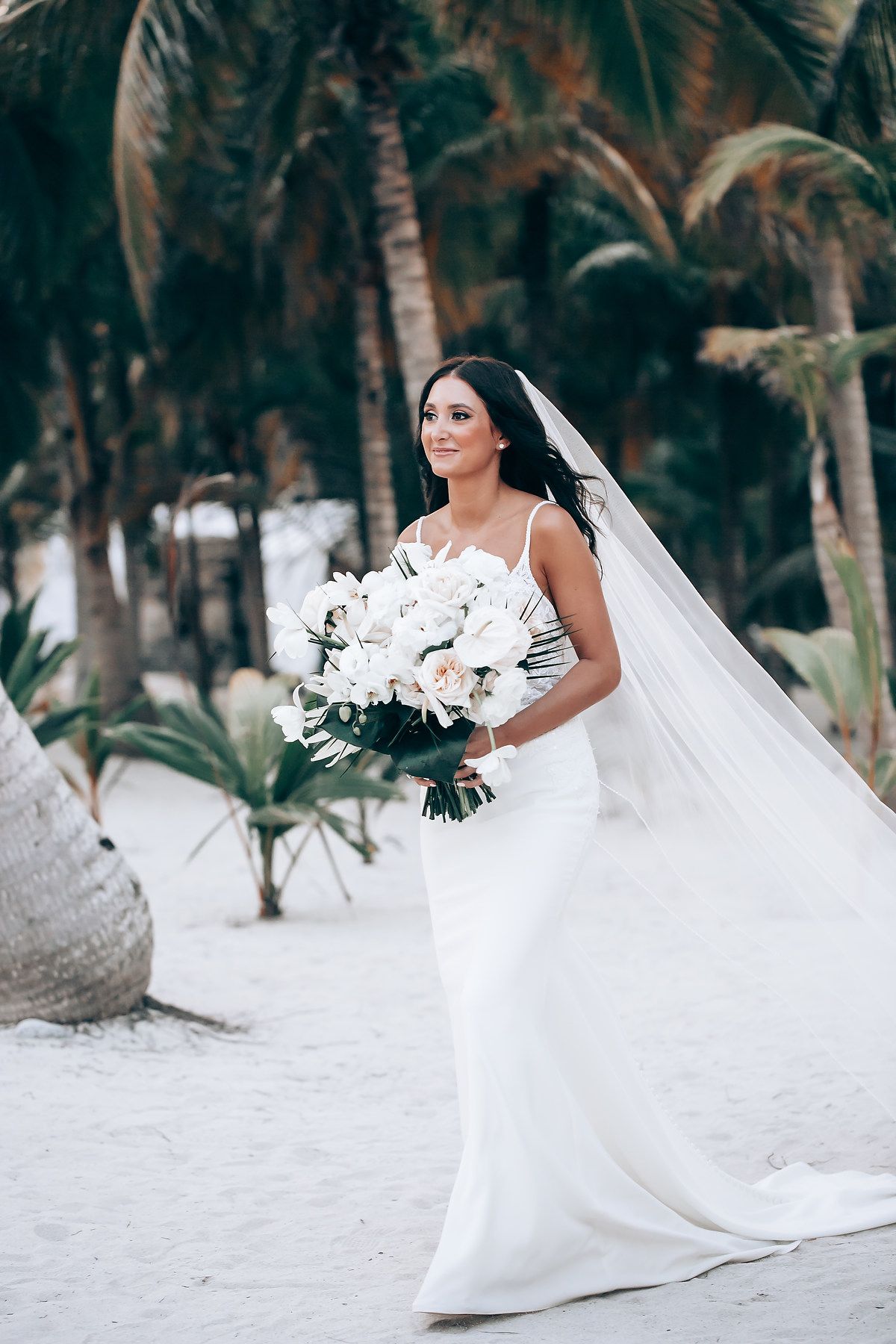 Elegant beach wedding photoshoot with white flowers and palm trees in the background.
