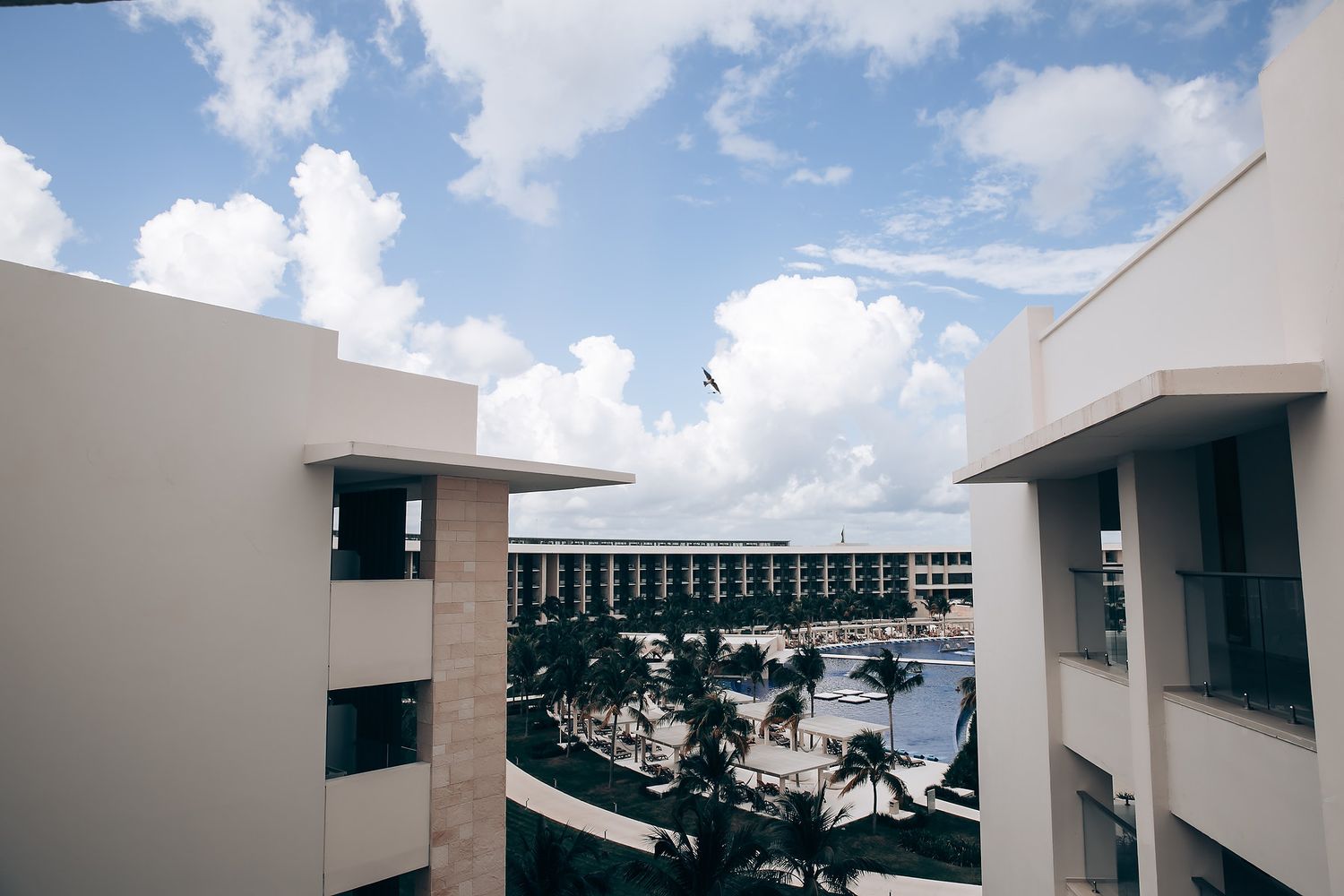 Modern white buildings with glass windows line a street under a bright blue sky with puffy white clouds.
