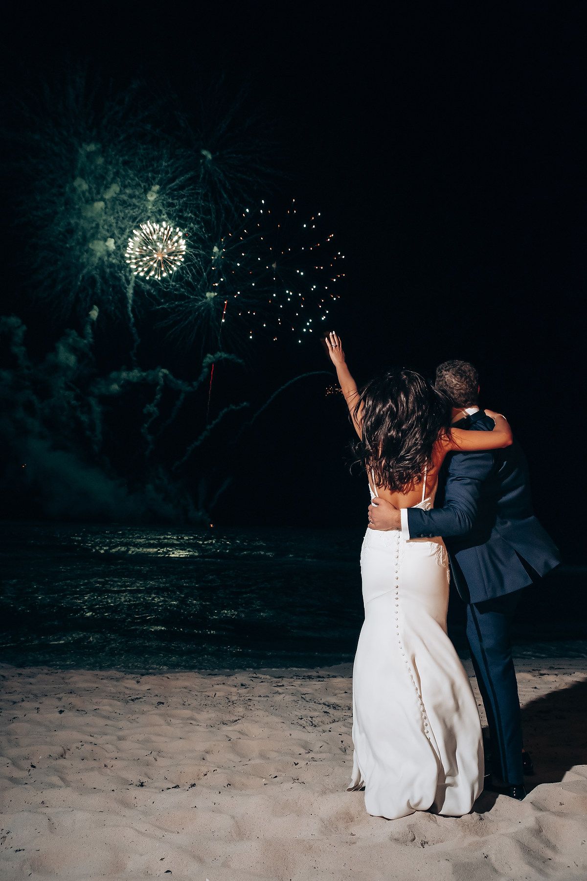 Couple watching fireworks display on beach during nighttime celebration.