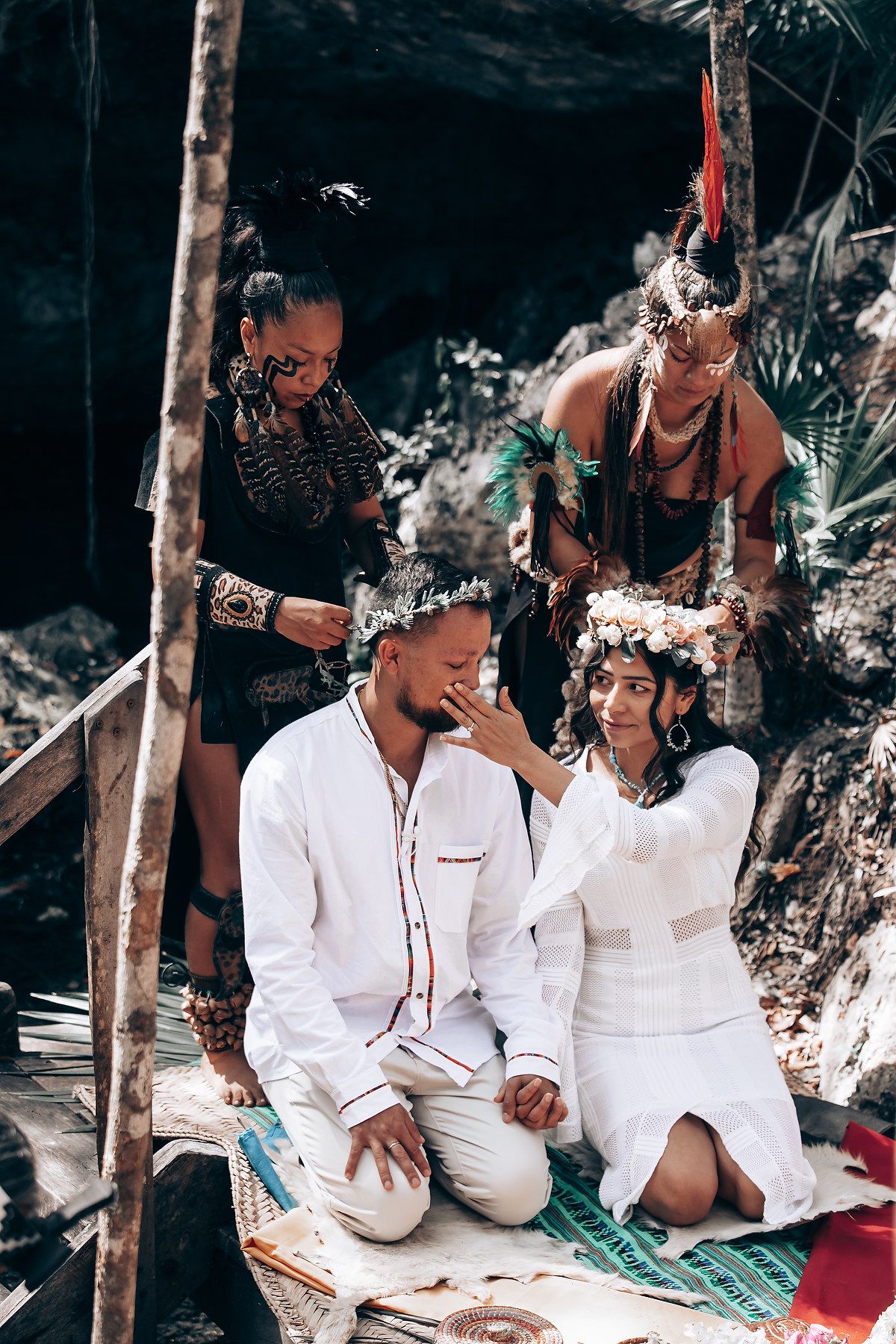 Group gathered on woven mats wearing white ceremonial clothing in a natural setting.