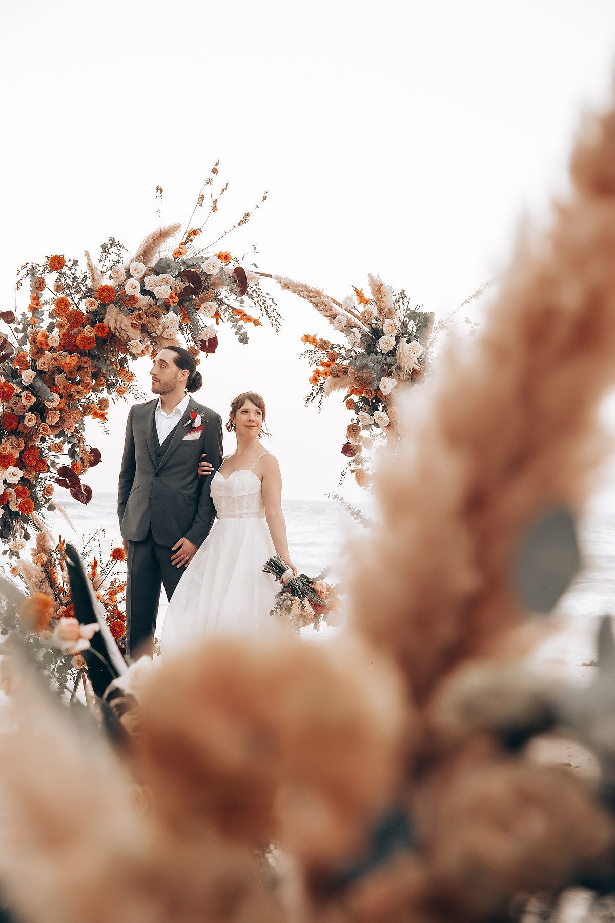 Wedding ceremony arch decorated with autumn-colored florals and white fabric.