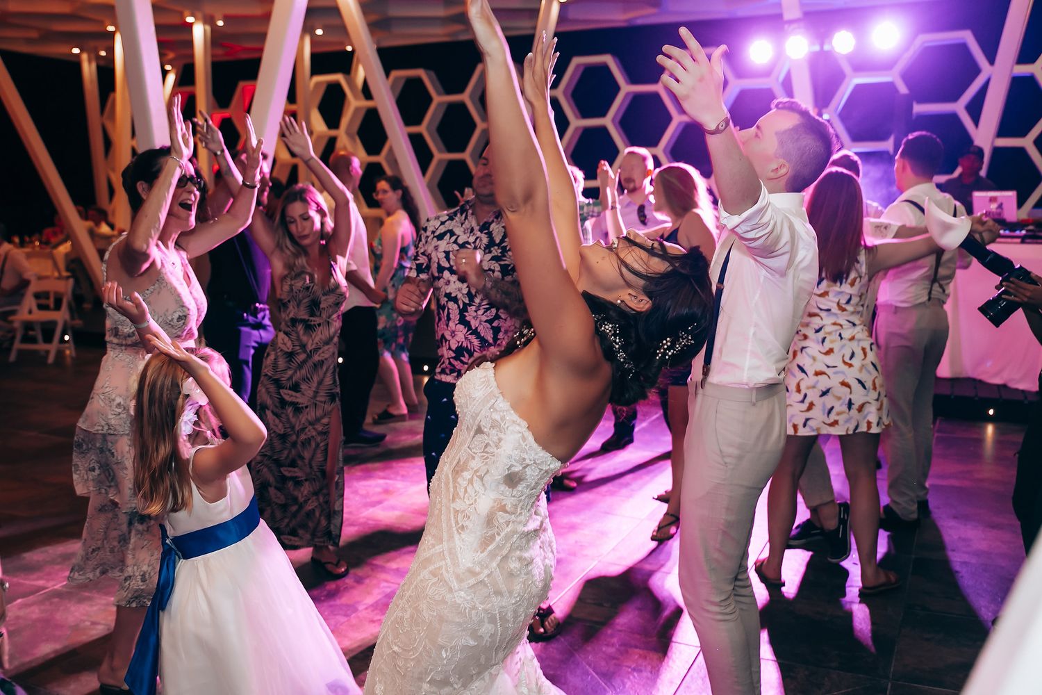 Wedding guests dancing under purple lighting at evening reception party.