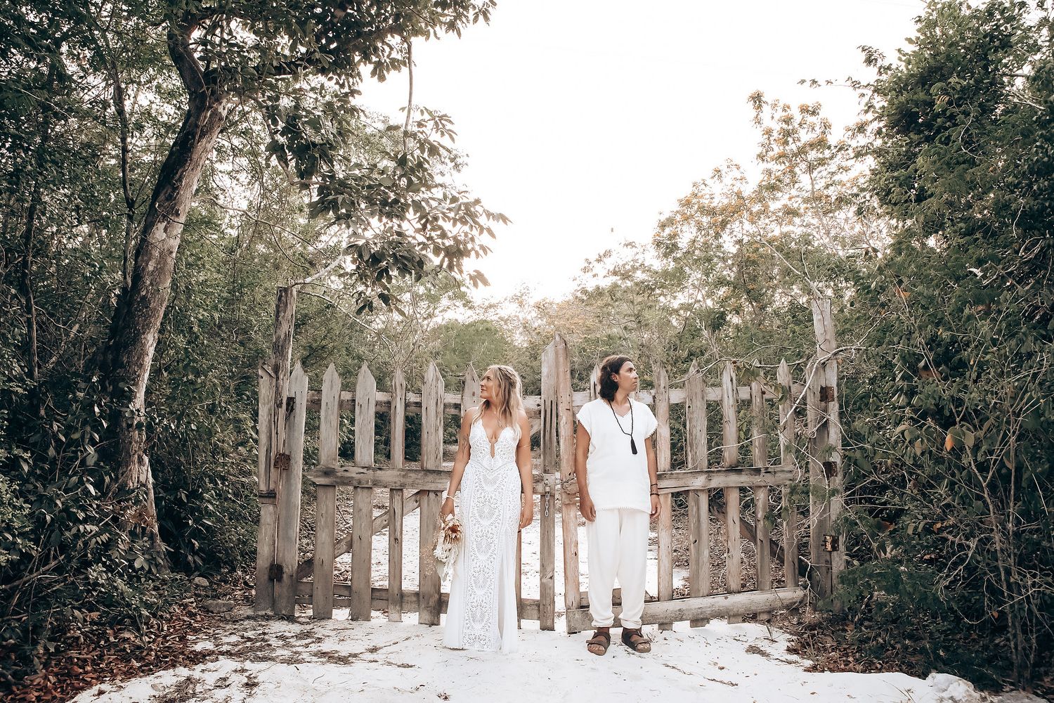 Wedding party in white dresses walking down a tree-lined path at an outdoor venue.